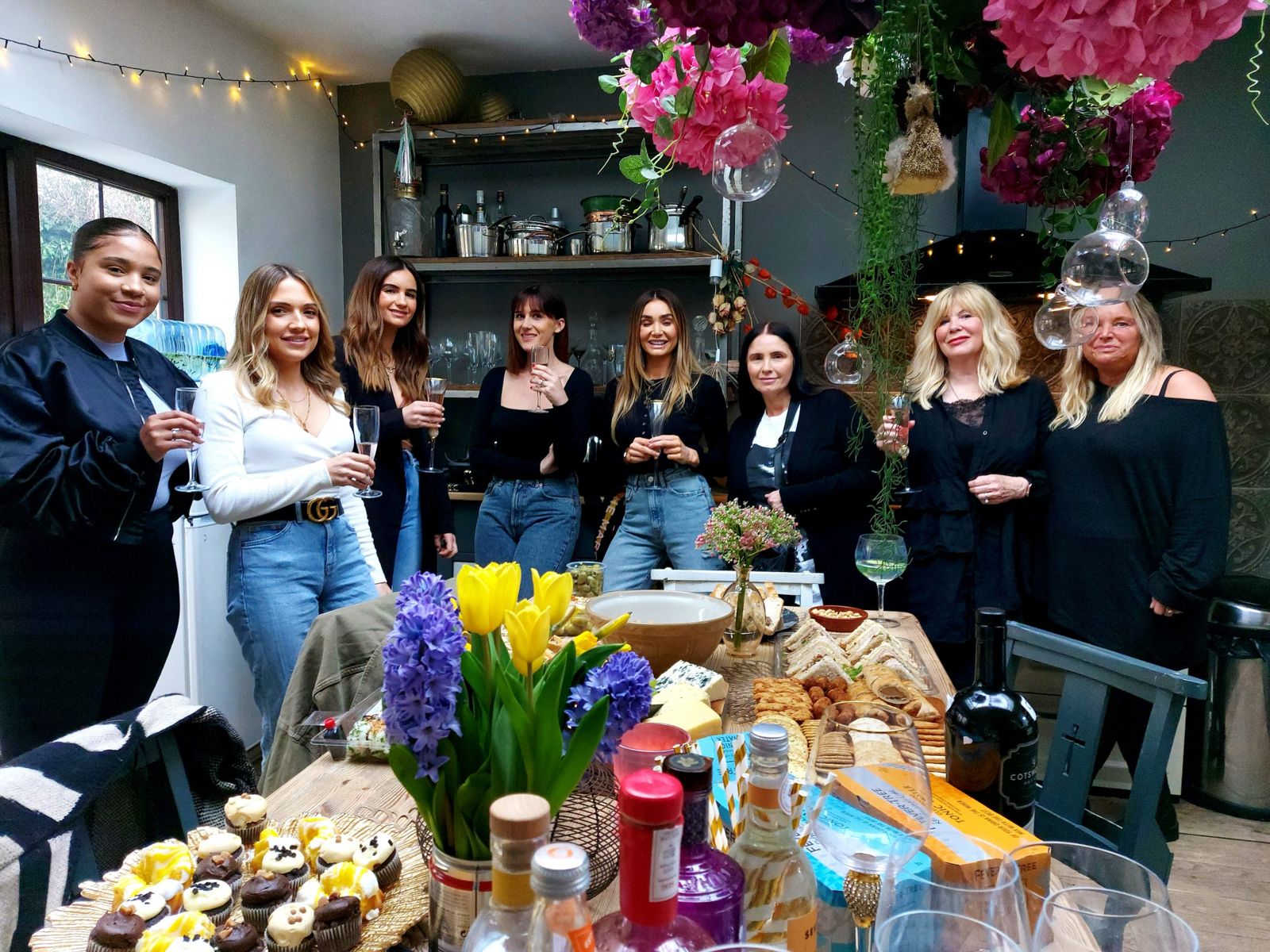 Guests with drinks around a table of food at an evening with Nikki