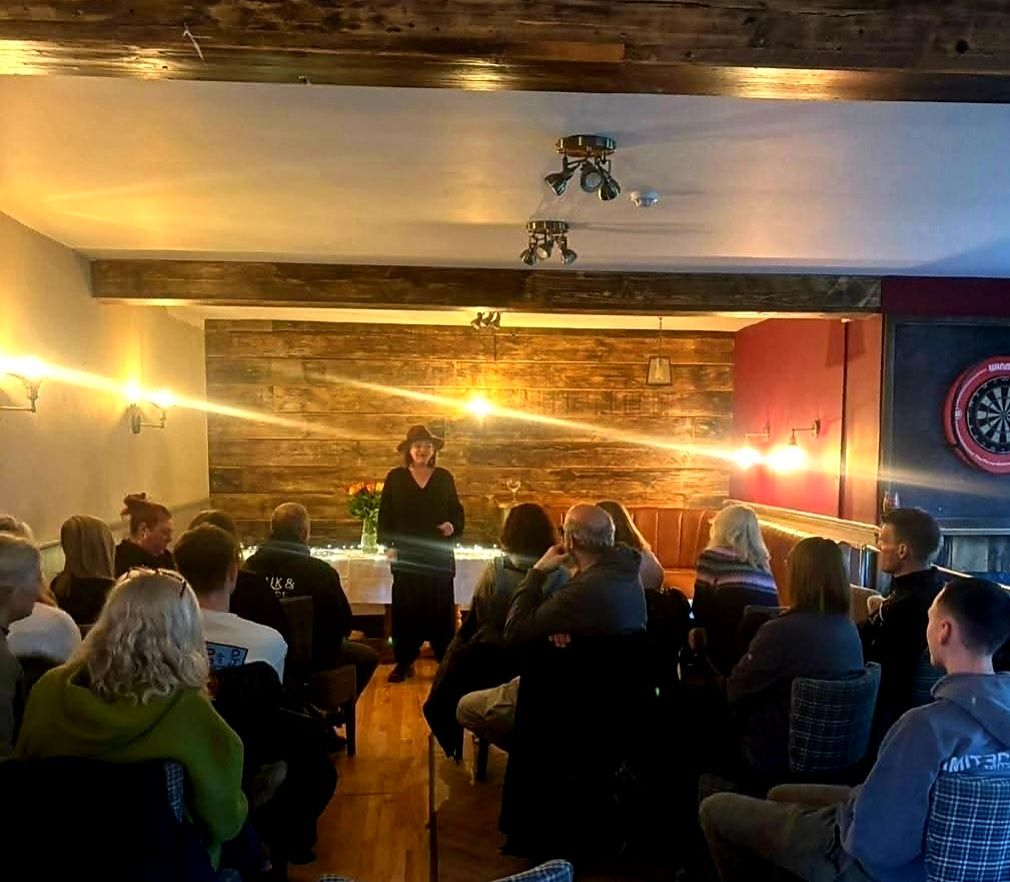 Nikki in her hat reading to a full room at a pub event